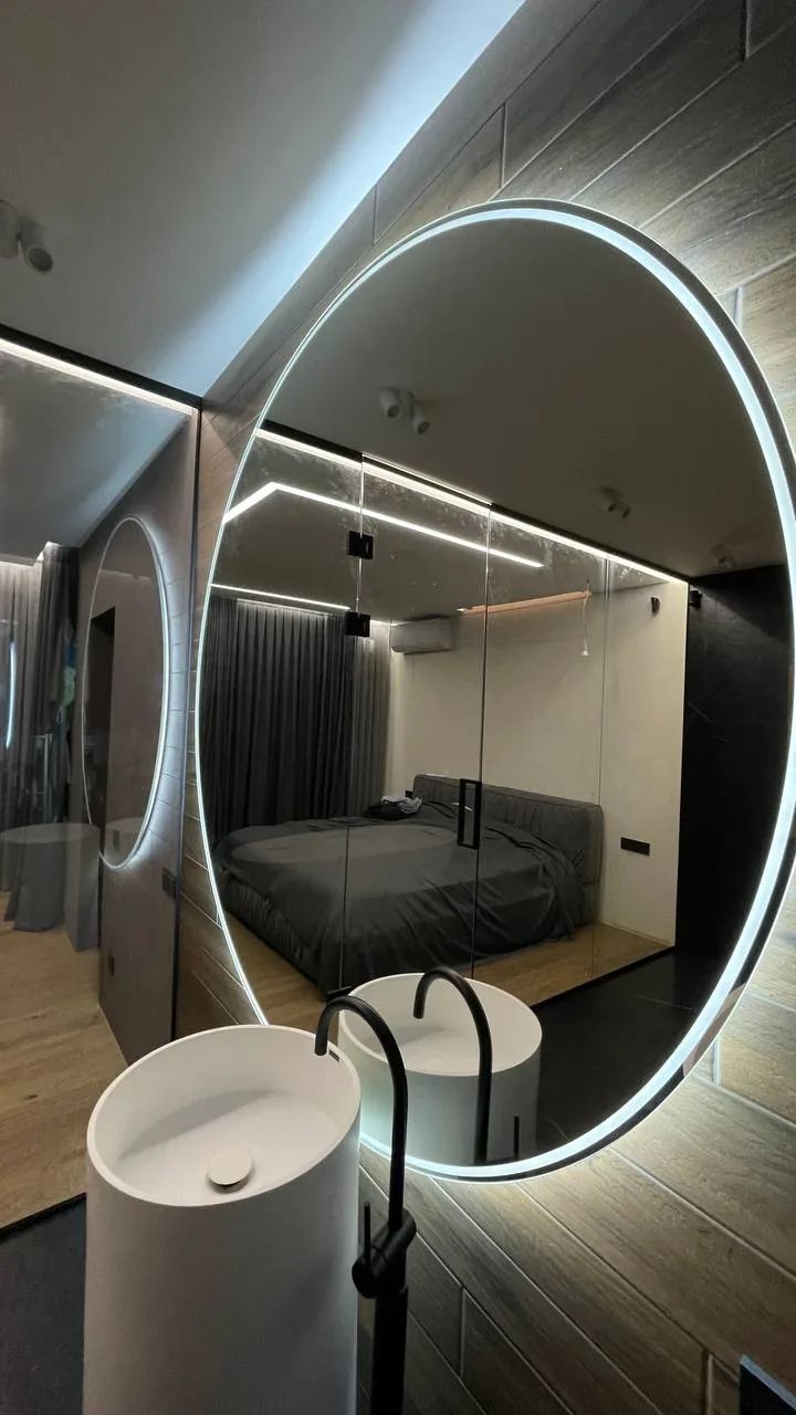 Large round backlit mirror reflecting a bedroom
