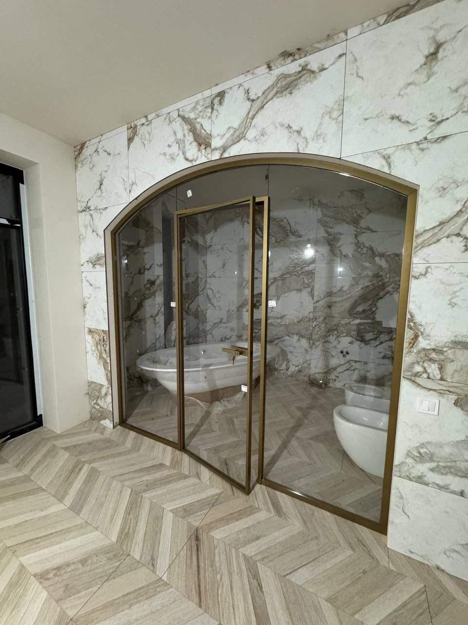 Arched glass partition in a gold-coloured profile in front of a marble bathroom